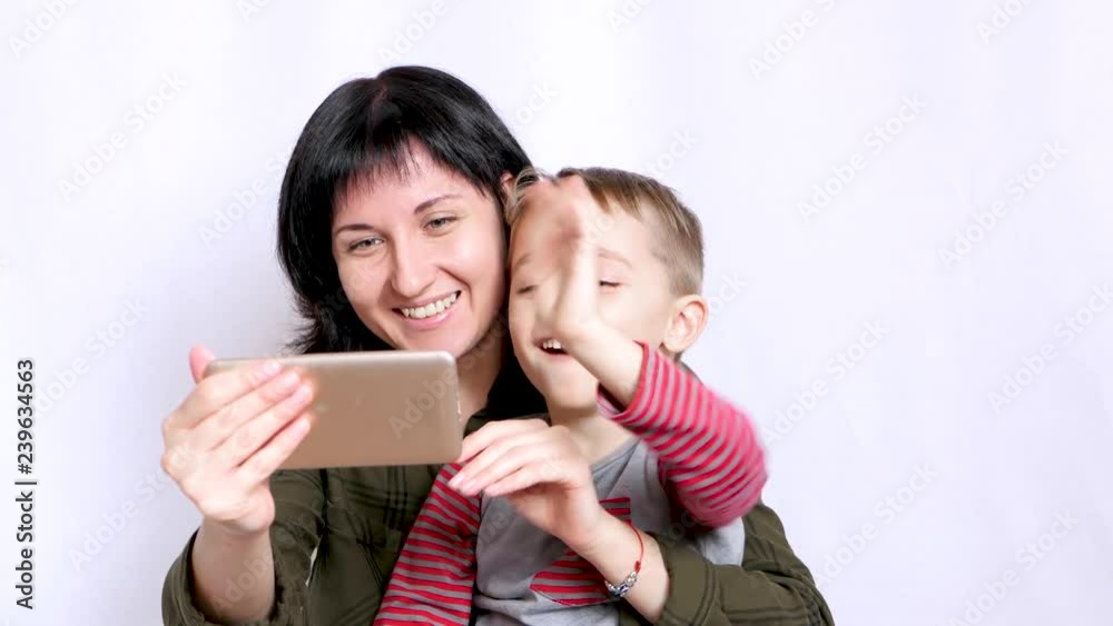 A happy young mother and child are looking at the screen of a smartphone and waving their hands while communicating on the Internet. Woman and little boy are laughing close up. A happy young mother and child are looking at the screen of a smartphone and waving their hands while communicating on the Internet. Woman and little boy are laughing close up.