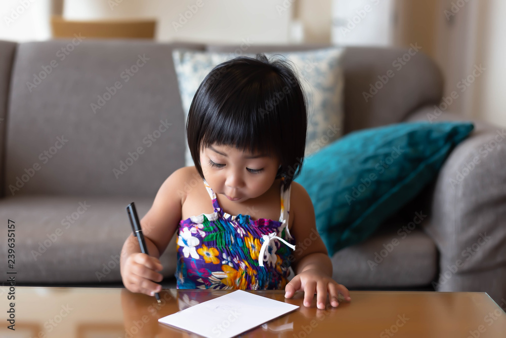 Adorable Little asian girl uses pen for writing on paper in living room at home. Pretty little child gets exciting and says wow with funny face. Toddler looks innocent and so cute Adorable Little asian girl uses pen for writing on paper in living room at home. Pretty little child gets exciting and says wow with funny face. Toddler looks innocent and so cute