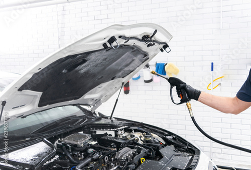 Car detailing. Manual car wash engine with pressure water. Washing car engine with water nozzle. Car washman worker cleaning vehicle engine. Man spraying pressure washer for car wash. photo