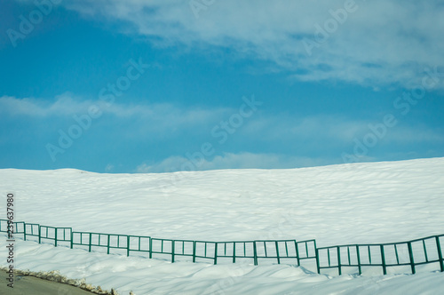 Reeling Fence on the edge of a road in a snow landscape with cloudy blue skies