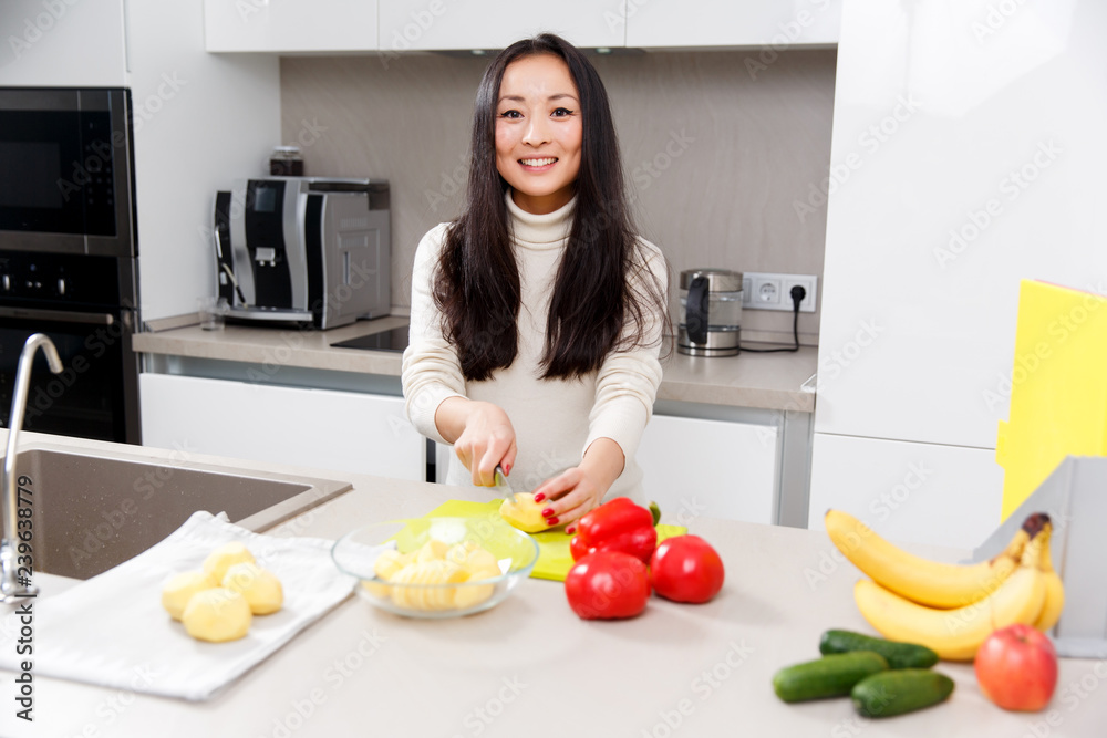 Picture of happy brunette cutting potatoes at table with vegetables and fruits