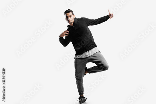 Stylish young man wearing a black sweatshirt and gray pants is dancing street dances on a white background