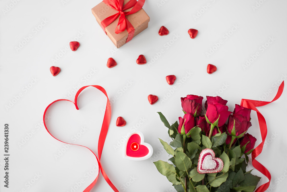 valentines day and holidays concept - close up of red roses, gift, red heart shaped chocolate candies and burning candle valentines day and holidays concept - close up of red roses, gift, red heart shaped chocolate candies and burning candle