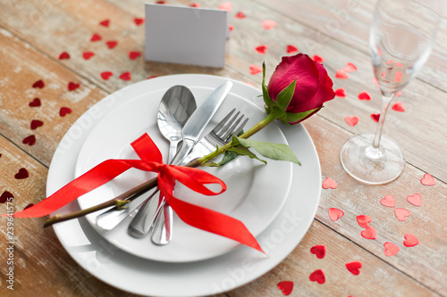 valentines day, table setting and romantic dinner concept - close up of red rose flower on set of dishes with cutlery, hearts and blank place card