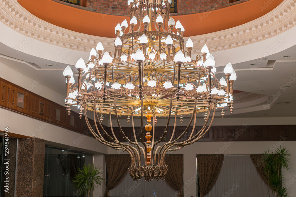 Huge chandelier in the hall. Chandelier on decoarted ceiling of a ballroom