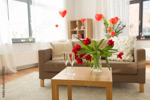 valentines day, romantic date and holidays concept - two champagne glasses and red tulip flowers on table in living room or home