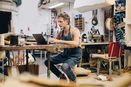 Male upholsterer using laptop in workshop photo