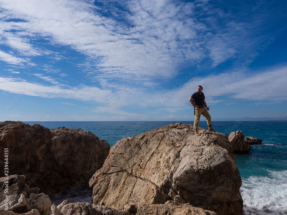 Young standing man on rock. the seashore at colorful sky. Beautiful landscape with sporty man rocks sea and sky at morning