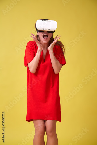 Girl in red dress and VR glasses  isolated on yellow background. Christmas or birthday emotions concept