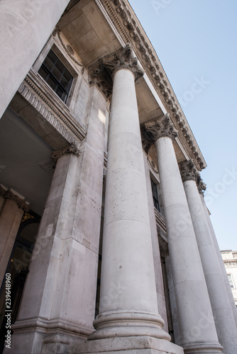 Large white columns of an old architectural building exterior. The building seems to have a brilliant architecture and is pretty old. The clear blue sky can be seen on the background.