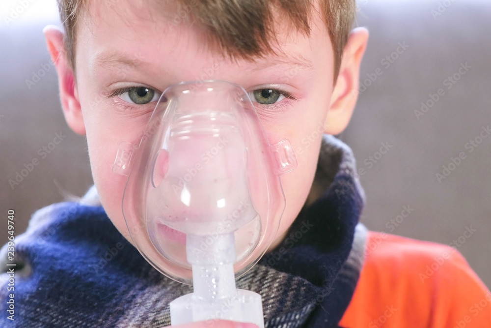 Sick blond boy inhaling through inhaler mask. Use nebulizer and inhaler for the treatment.