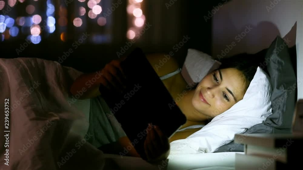 Happy teen browsing and watching media in a tablet lying in the bed in the night at home