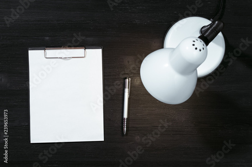 Blank paper page document with copy space and lamp on the black office table background. To do list. Resume form. Estimate.