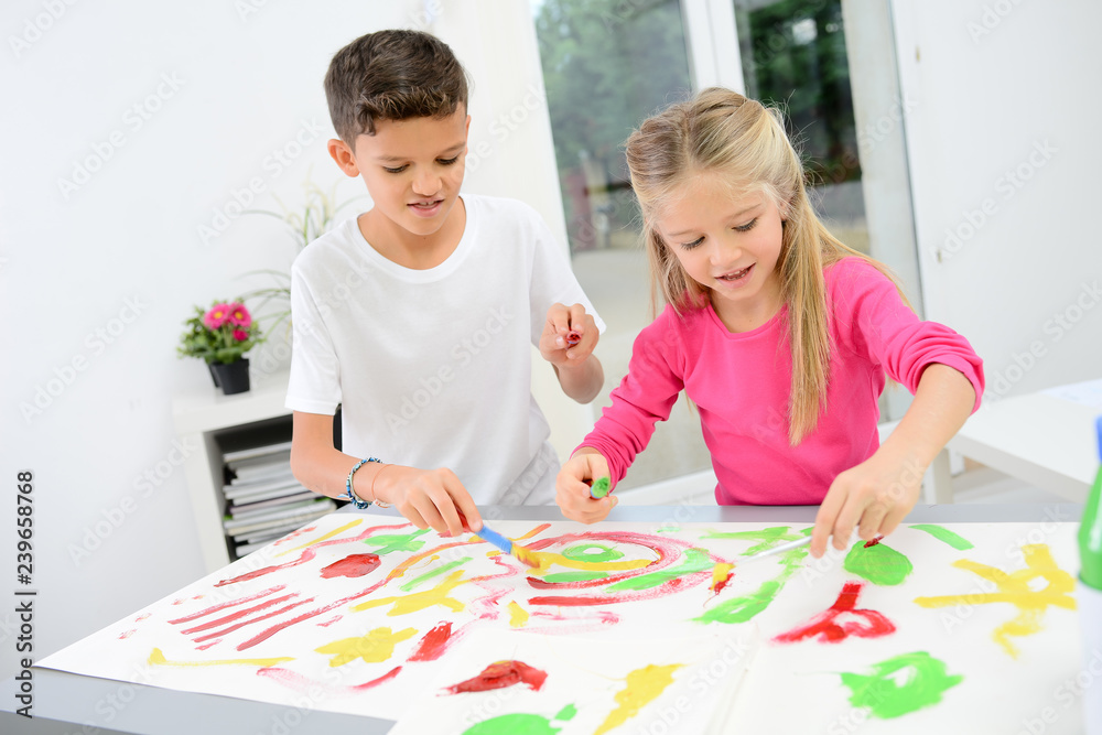 Fototapeta premium two beautiful young kids boy and girl hand painting on a white paper with color paint