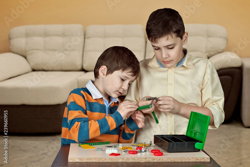 Two boys are played by a designer on the table. Two brothers make a metal designer with bolts and nuts.
