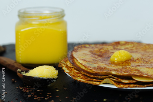 Pancakes roasted on a tray are plentifully covered with butter and a wooden spoon with butter photo