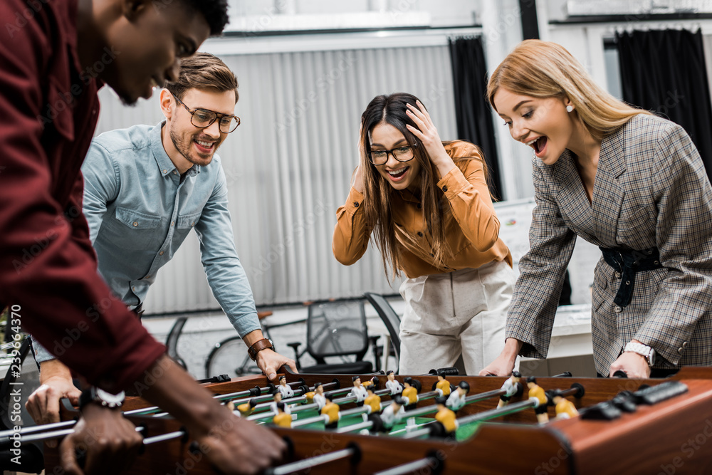 Fototapeta premium emotional multicultural business colleagues playing table football together in office