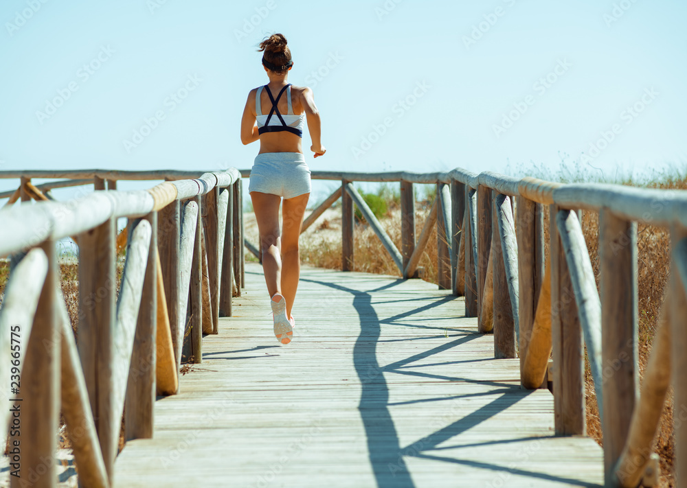 active sports woman in sport clothes on ocean coast jogging - obrazy, fototapety, plakaty 