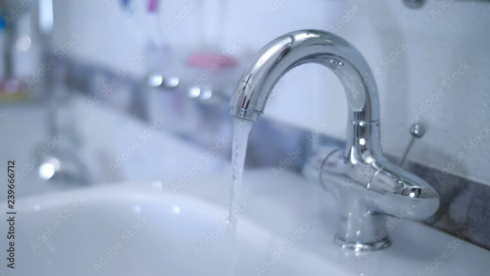 In the bathroom, the hand opens ( closing ) the water tap and water starts to flow from the faucet into the washbasin. Closeup In the bathroom, the hand opens ( closing ) the water tap and water starts to flow from the faucet into the washbasin. Closeup