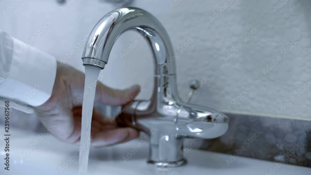 In the bathroom, the hand opens ( closing ) the water tap and water starts to flow from the faucet into the washbasin. Closeup. Shot in motion In the bathroom, the hand opens ( closing ) the water tap and water starts to flow from the faucet into the washbasin. Closeup. Shot in motion