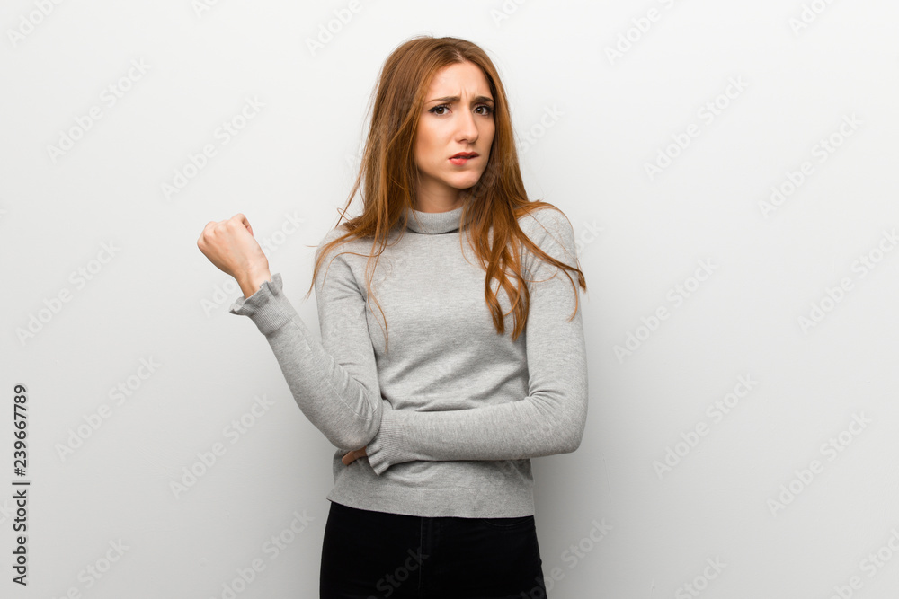 Redhead girl over white wall with confuse face expression while bites lip Redhead girl over white wall with confuse face expression while bites lip