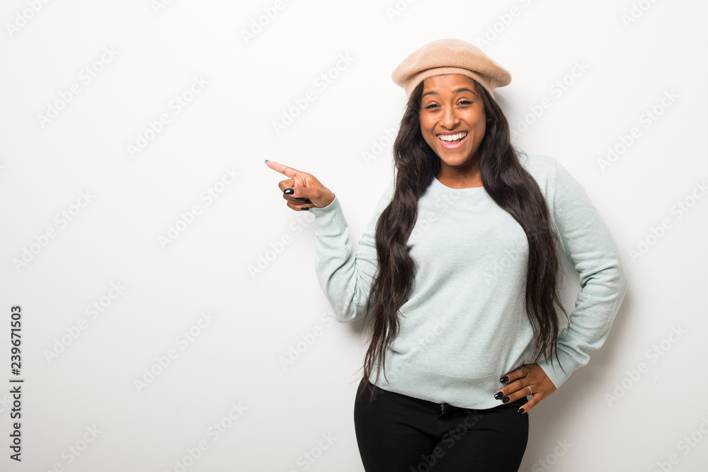 Young afro american woman on white wall pointing finger to the side and presenting a product while smiling Young afro american woman on white wall pointing finger to the side and presenting a product while smiling