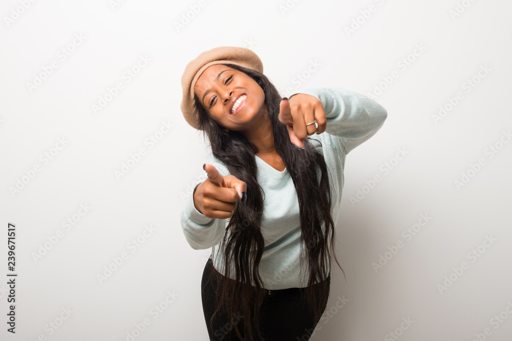 Young afro american woman on white wall points finger at you while smiling Young afro american woman on white wall points finger at you while smiling
