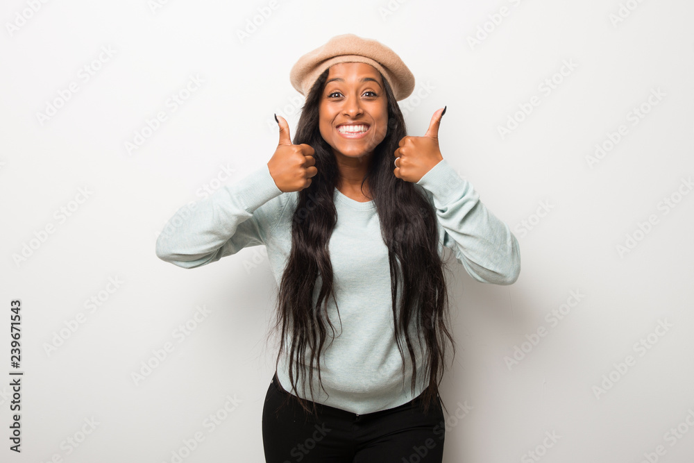 Young afro american woman on white wall giving a thumbs up gesture and smiling because has had success Young afro american woman on white wall giving a thumbs up gesture and smiling because has had success