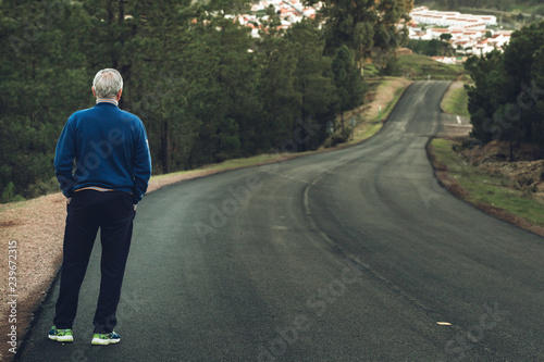 Active senior man standing on lonely road between mountains