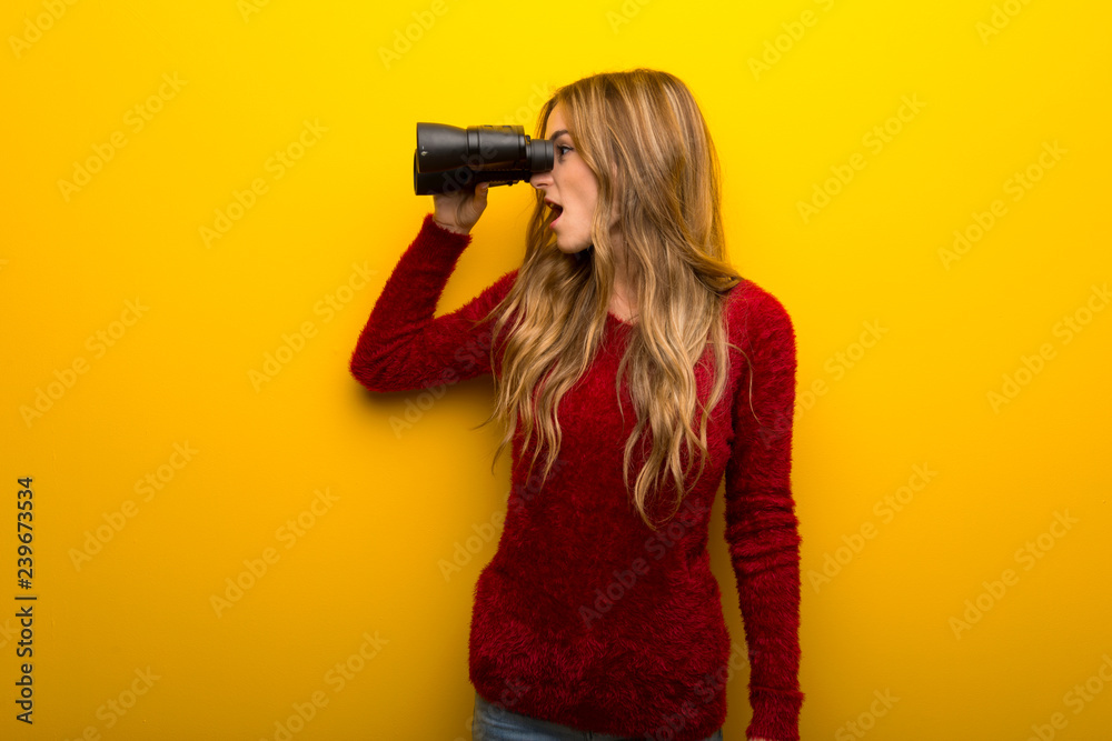 Young girl on vibrant yellow background and looking in the distance with binoculars