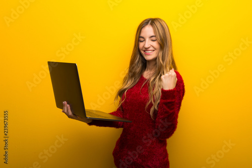 Young girl on vibrant yellow background with laptop and celebrating a victory