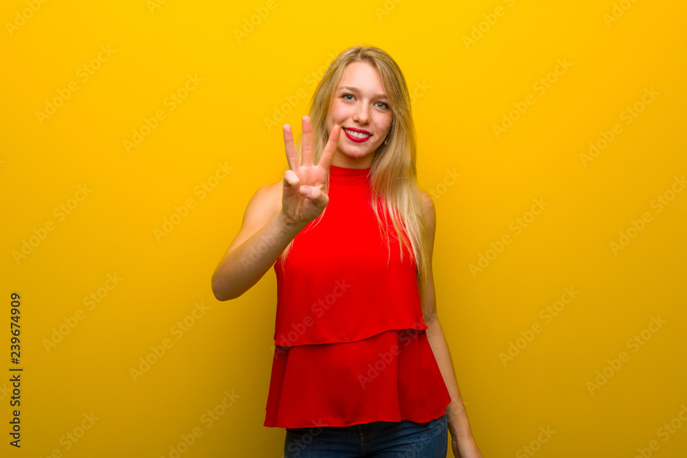 Young girl with red dress over yellow wall happy and counting three with fingers Young girl with red dress over yellow wall happy and counting three with fingers