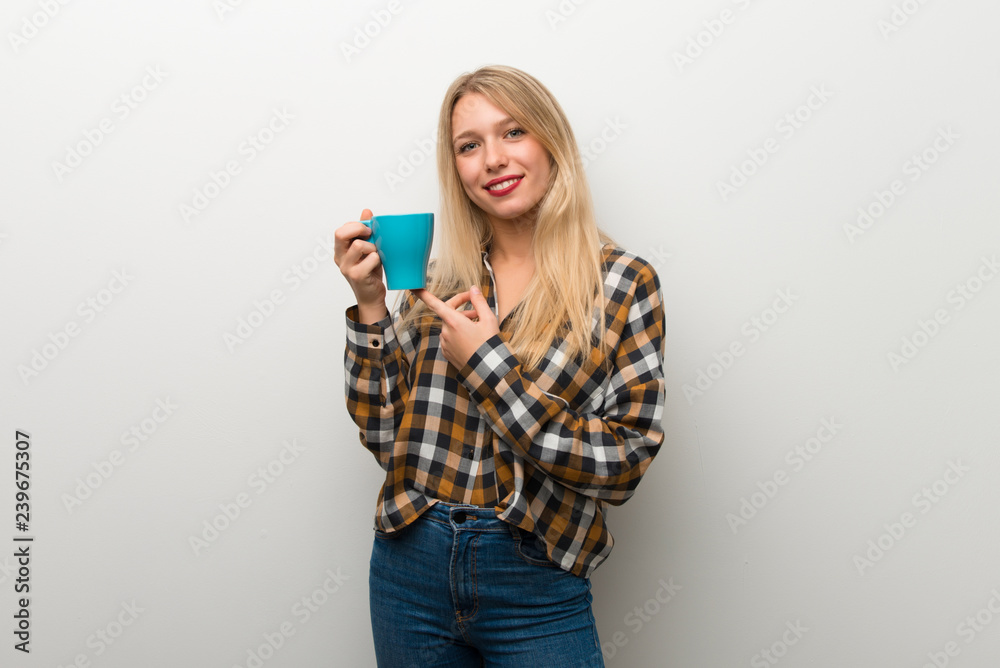 Blonde young girl over white wall holding a hot cup of coffee Blonde young girl over white wall holding a hot cup of coffee