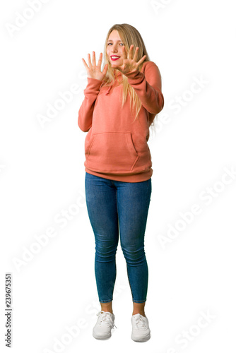 A full-length shot of a Young girl is a little bit nervous and scared stretching hands to the front on isolated white background © luismolinero