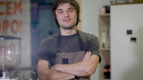 funny handsome barista young man is posing for a camera in a bar, crossing hands and grimacing jokingly photo