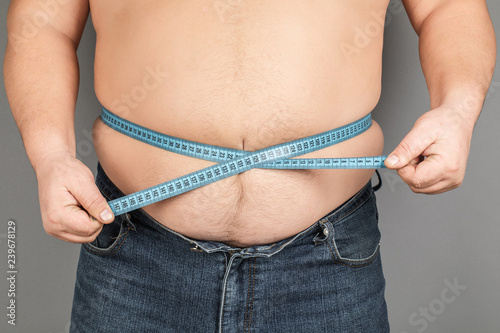 A man measures his fat belly with a measuring tape. on a gray background.