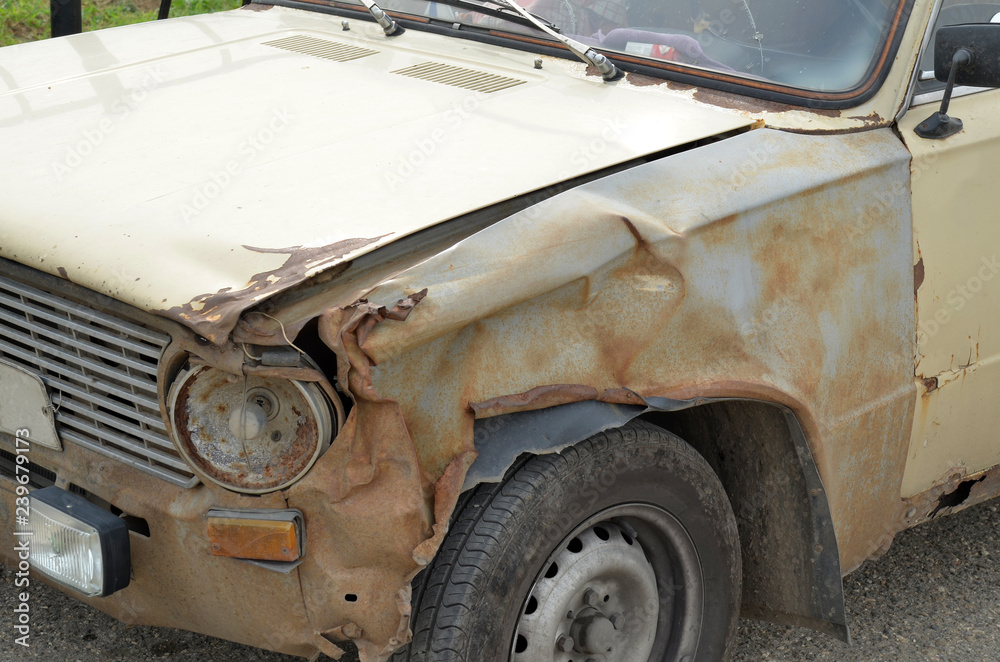 Fragment of the front part of an old rusty broken car that has  been in an accident. Peeling paint, broken headlight