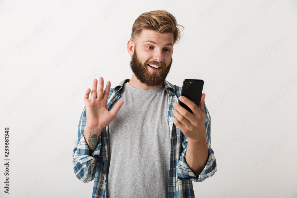 Handsome young bearded man standing isolated over white wall background using mobile phone. Handsome young bearded man standing isolated over white wall background using mobile phone.