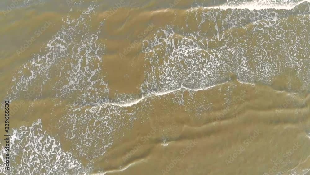 Aerial Top view. The wave arrives to the shore and breaks down over the sand and muds the sea water Aerial Top view. The wave arrives to the shore and breaks down over the sand and muds the sea water