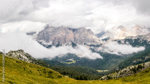 High rocky peaks and a wooded valley in fog and white clouds in Dolomites, South Tyrol, Italy