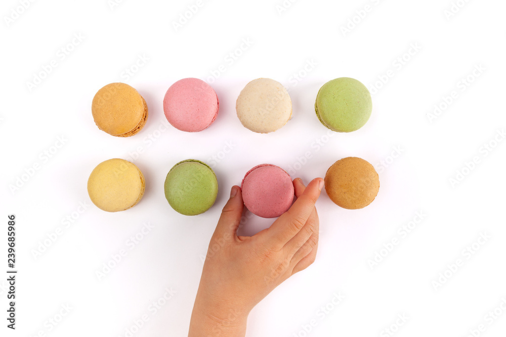 Girl's hand taking pink French macaron from two rows of colorful macarons isolated on white Girl's hand taking pink French macaron from two rows of colorful macarons isolated on white