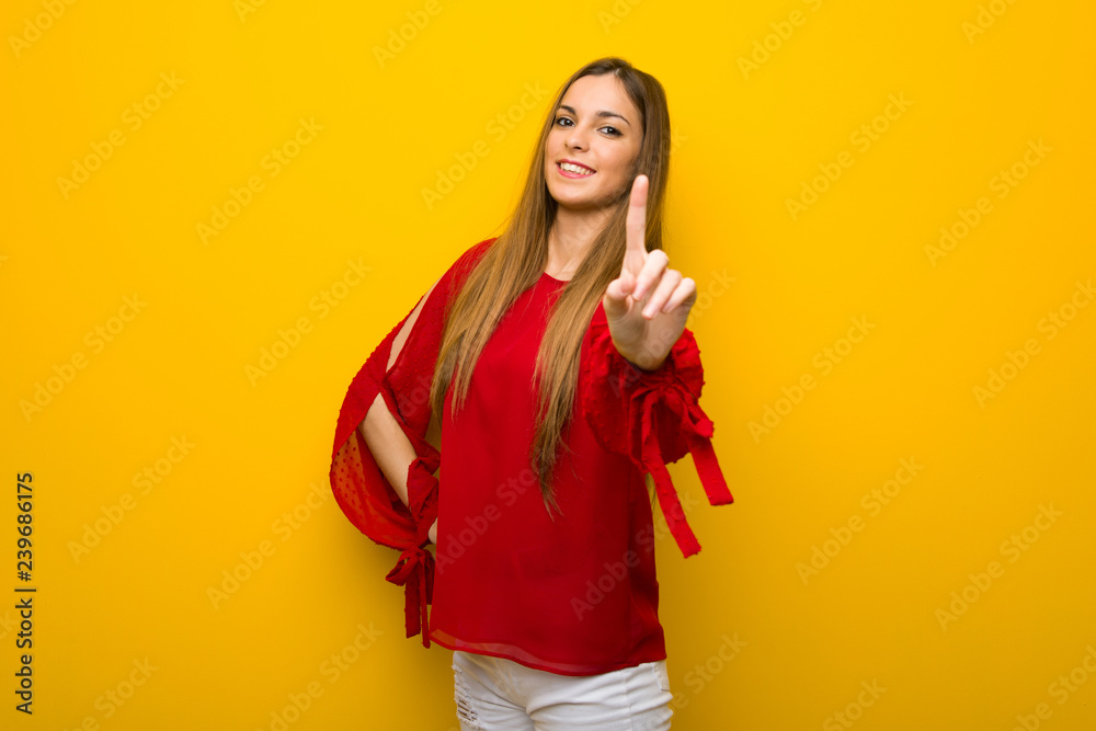 Young girl with red dress over yellow wall showing and lifting a finger Young girl with red dress over yellow wall showing and lifting a finger
