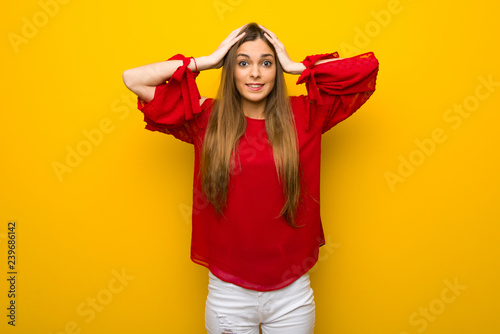 Young girl with red dress over yellow wall takes hands on head because has migraine