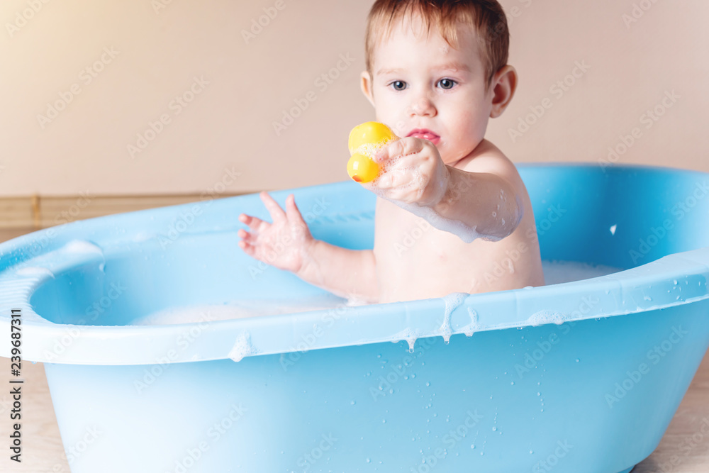 Cute boy washing in blue bath in bathroom. Baby is playing with a yellow duck and soap foam. Cute boy washing in blue bath in bathroom. Baby is playing with a yellow duck and soap foam.