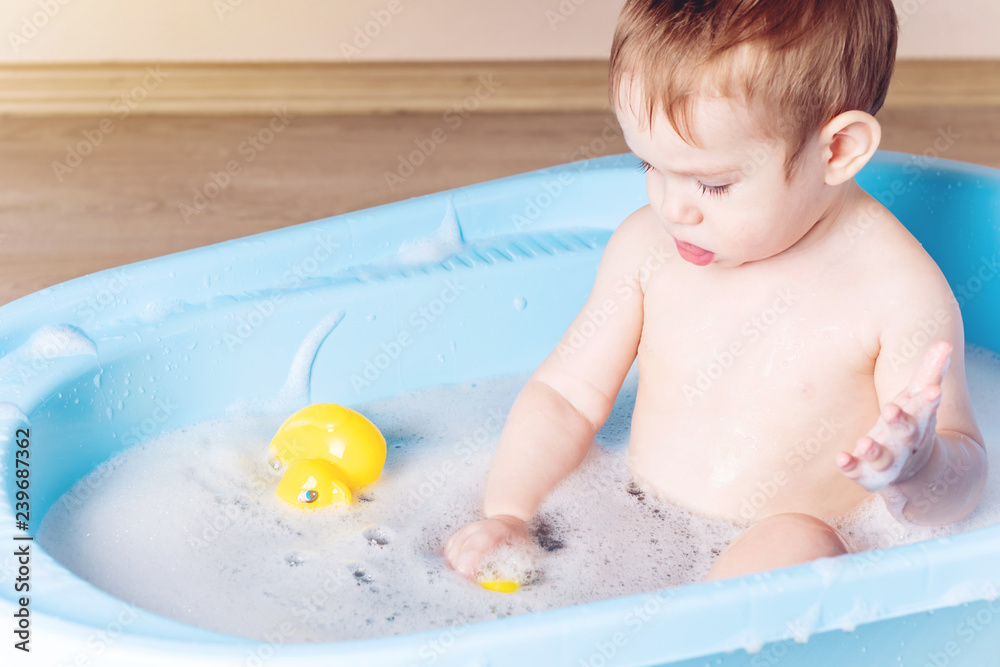 Cute boy washing in blue bath in bathroom. Baby is playing with a yellow duck and soap foam. Cute boy washing in blue bath in bathroom. Baby is playing with a yellow duck and soap foam.