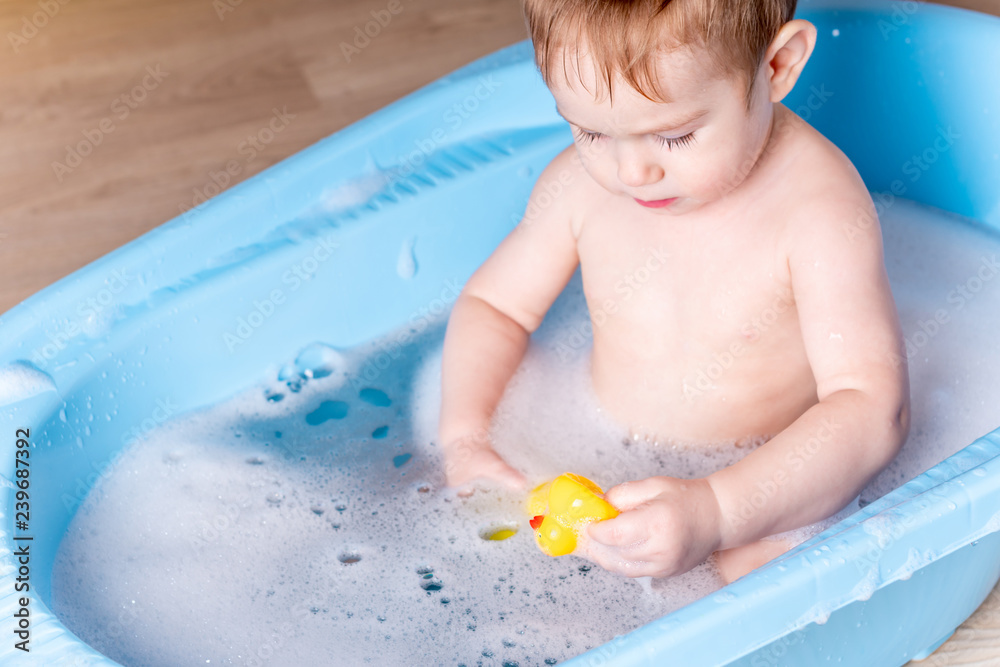 Cute boy washing in blue bath in bathroom. Baby is playing with a yellow duck and soap foam. Cute boy washing in blue bath in bathroom. Baby is playing with a yellow duck and soap foam.