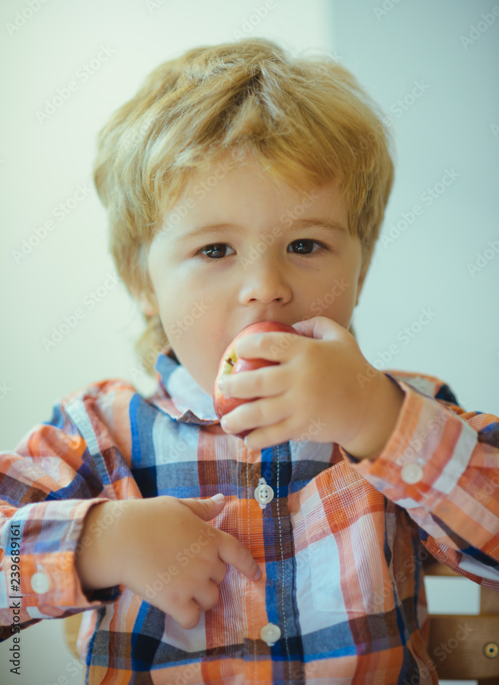 Portrait of a cute schoolboy with red apple on a white background. Little blond boy with red delicious apple fruit. Cute child portrait eating apple indoor. Portrait of a cute schoolboy with red apple on a white background. Little blond boy with red delicious apple fruit. Cute child portrait eating apple indoor.