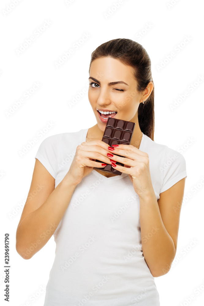 beautiful young happy brunette woman in white t-shirt holds chocolate and bites it, winking. on white background beautiful young happy brunette woman in white t-shirt holds chocolate and bites it, winking. on white background