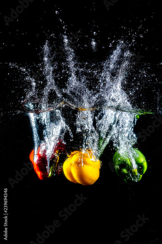 Fresh colourful bell pepper splashing in water on black background.