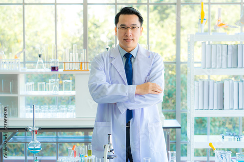A middle aged man scientist smiling happily with his arms crossed posing at her laboratory colleagues. A confident professor CEO standing preparing equipment for teaching collage student. Copy space.